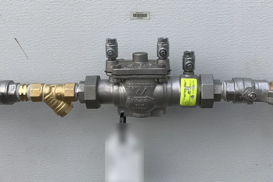 A stainless testable backflow preventer on a copper water line, with green-handled isolation valves either side, a brass strainer and test points on top