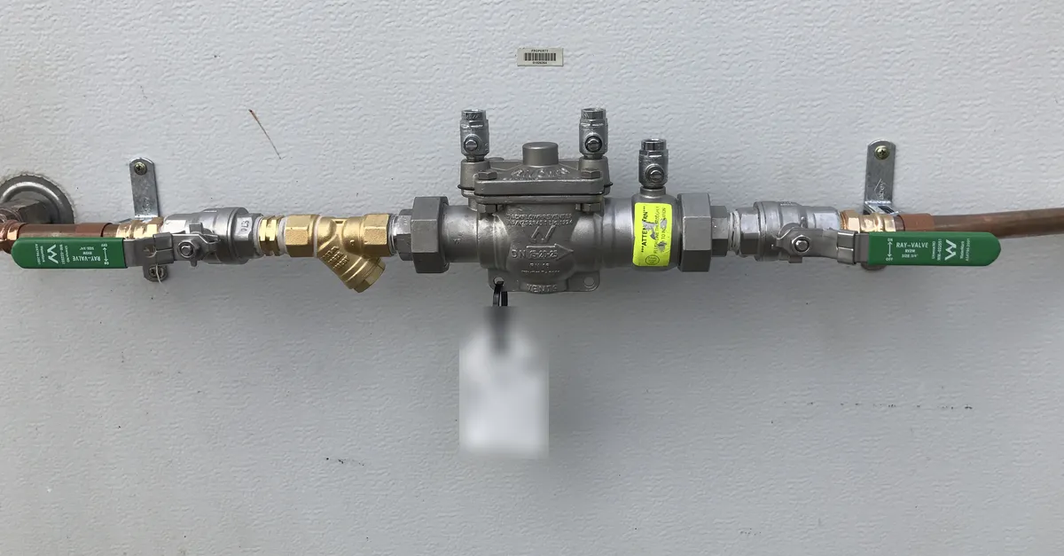 A testable backflow preventer with green-handled isolation valves on a copper line against a grey wall