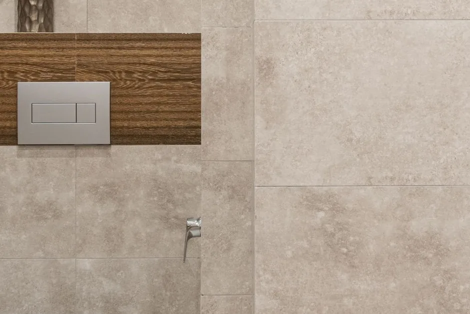 A chrome dual flush plate mounted on a tiled bathroom wall above a timber panel