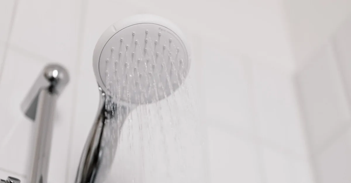 Water running from a chrome shower head in a white tiled bathroom