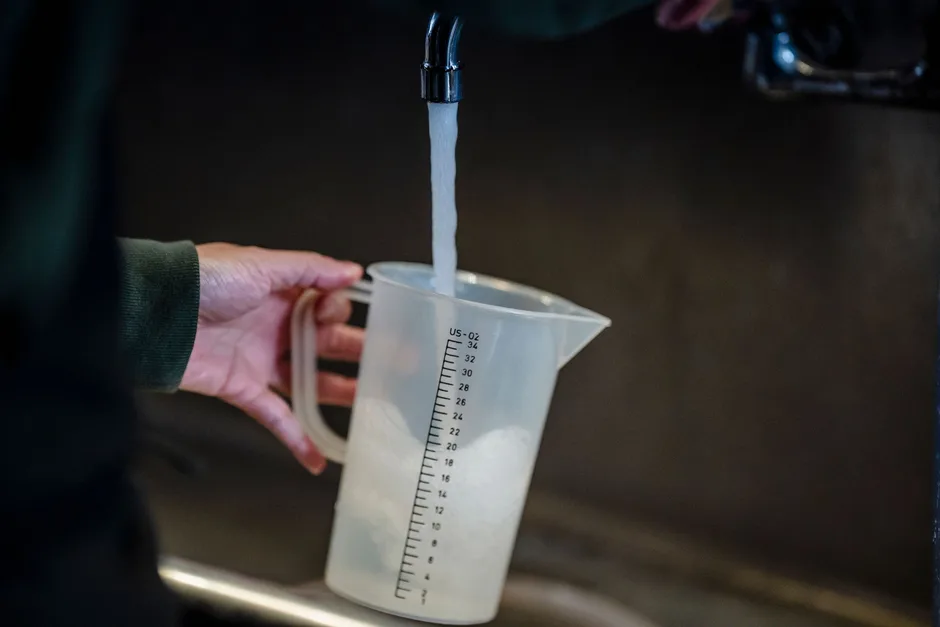 A hand holding a measuring jug under a running tap