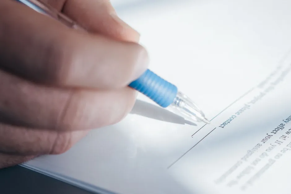 A hand signing a printed form with a blue pen