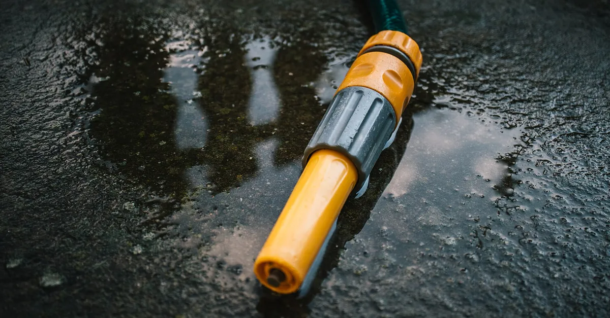 A garden hose with a yellow and grey shut-off nozzle lying on wet concrete