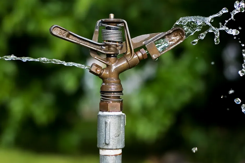 A brass impact sprinkler on a galvanised riser throwing jets of water across a garden