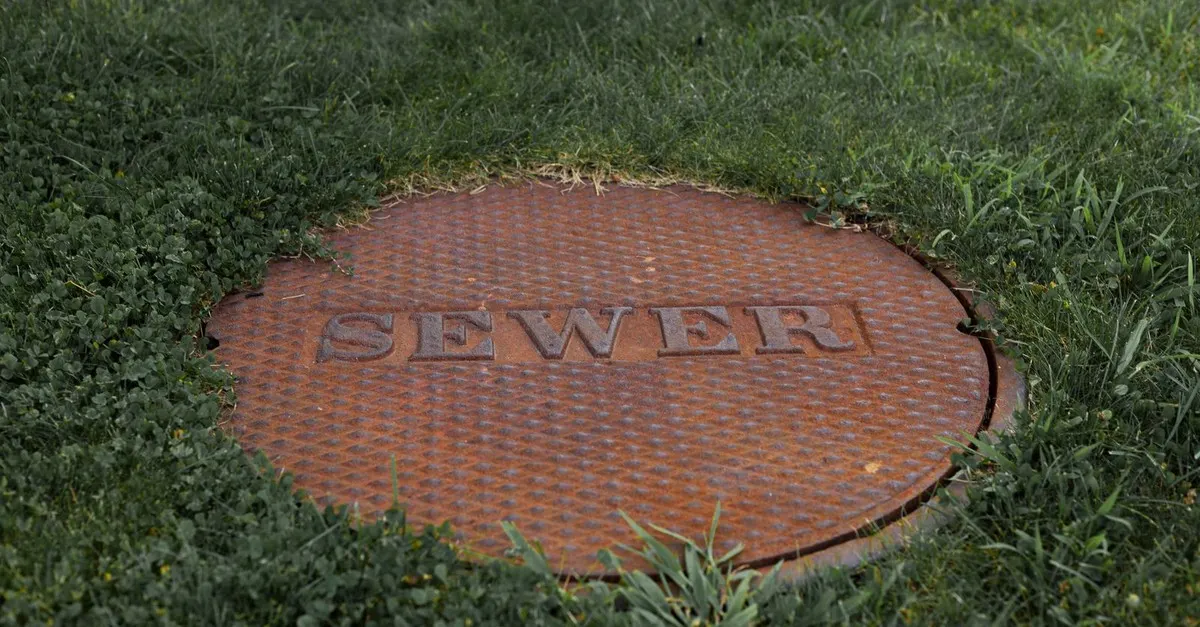 A rusted cast iron sewer maintenance hole cover set into a grass lawn