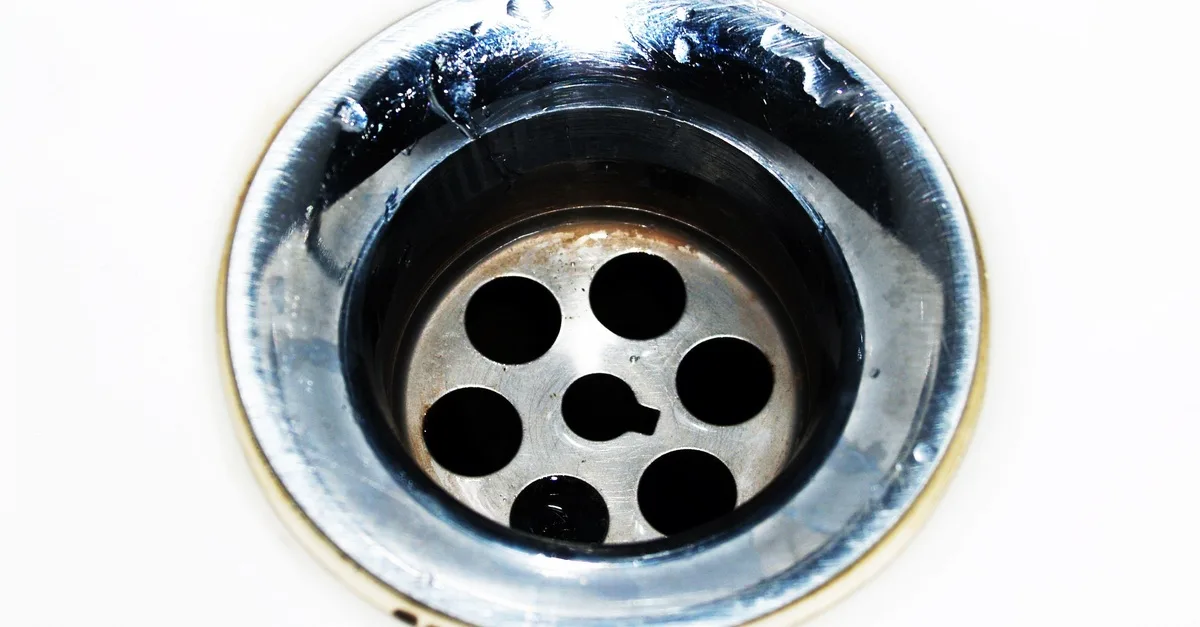 Close-up of a stained chrome waste outlet in a white basin