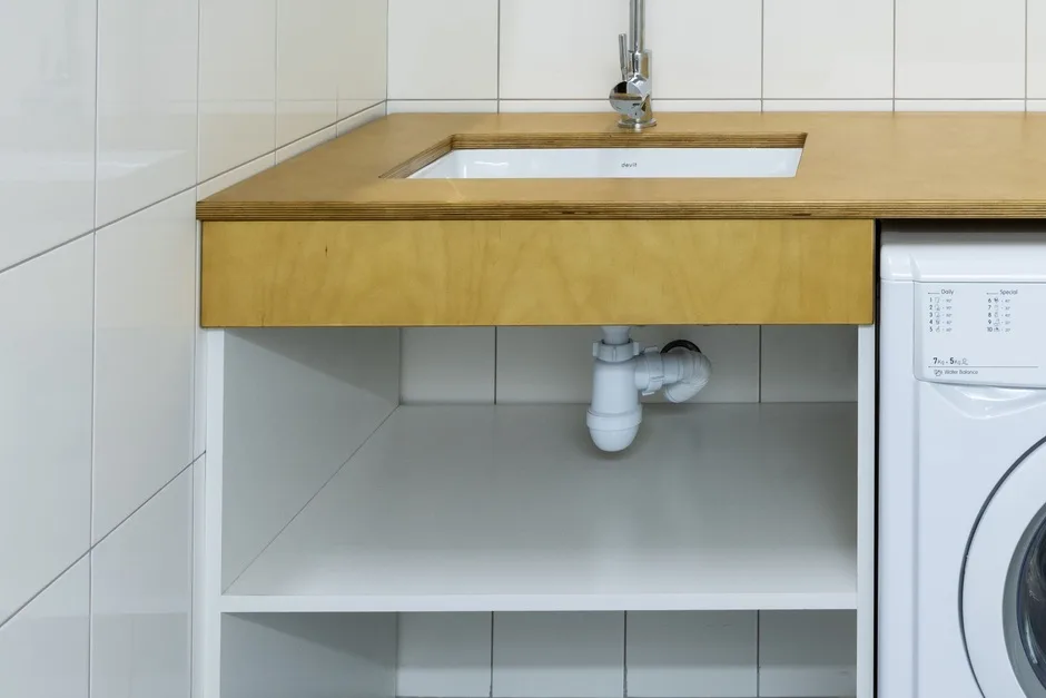 A white plastic trap under a laundry sink, with the bend that holds the water seal visible