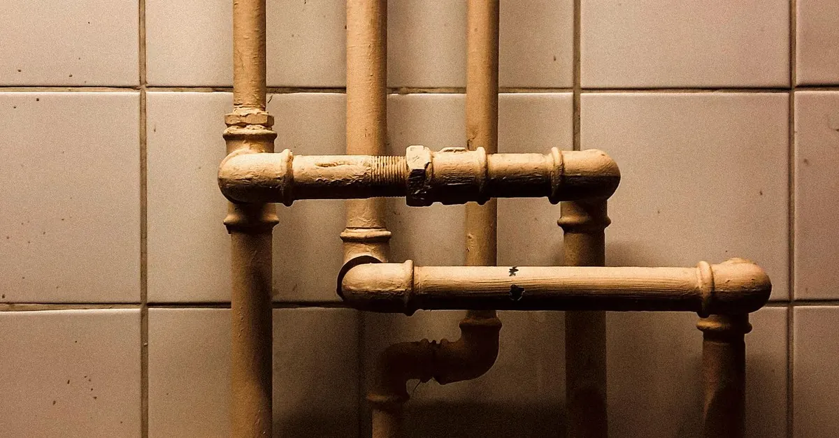 Painted service pipes rising up a tiled wall and branching off to different outlets