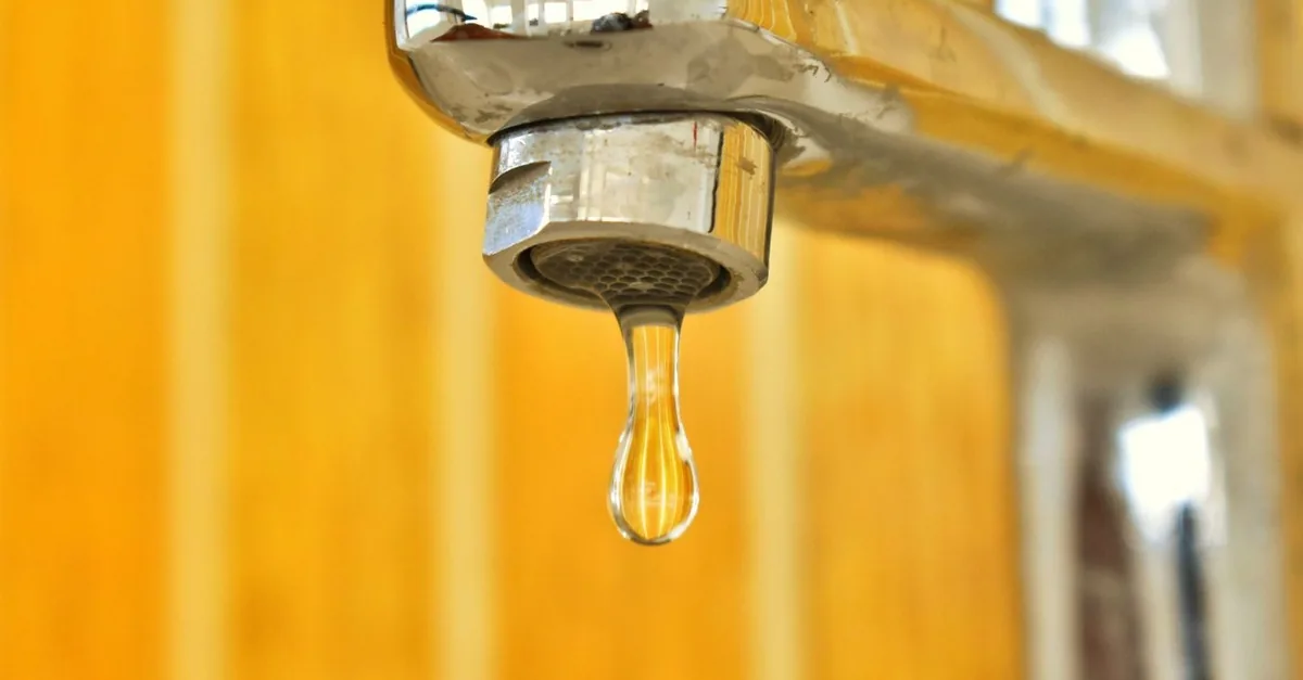 A chrome tap with a single drop of water hanging from the spout