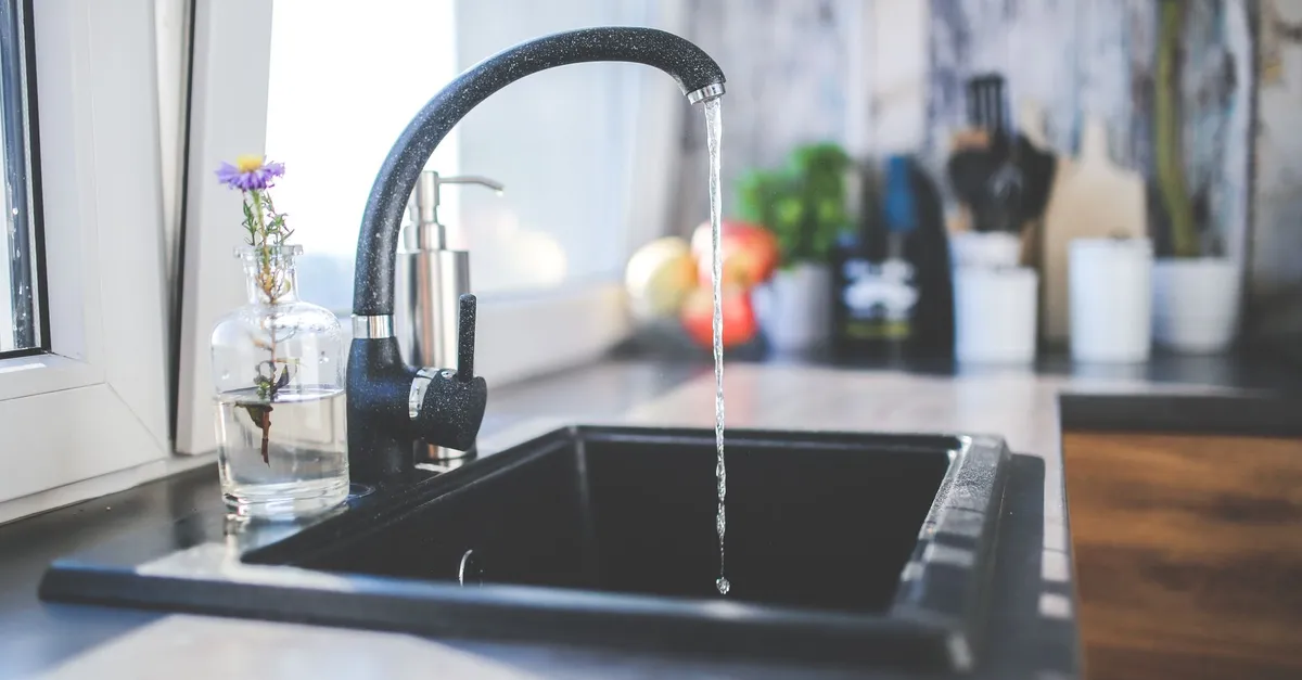 Water running from a black kitchen mixer tap into a dark sink beside a window