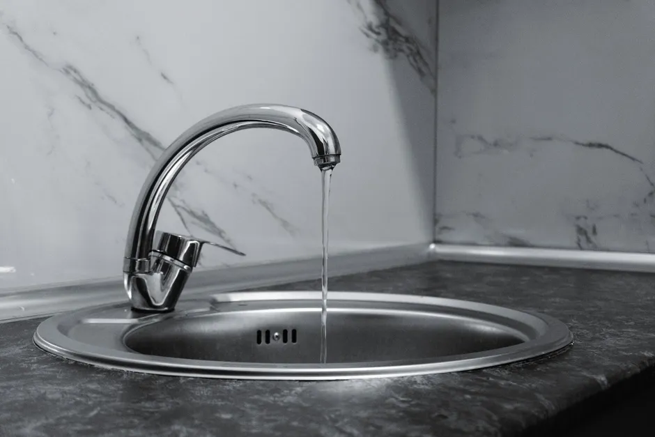 Cold water running from a chrome kitchen mixer into a round steel sink