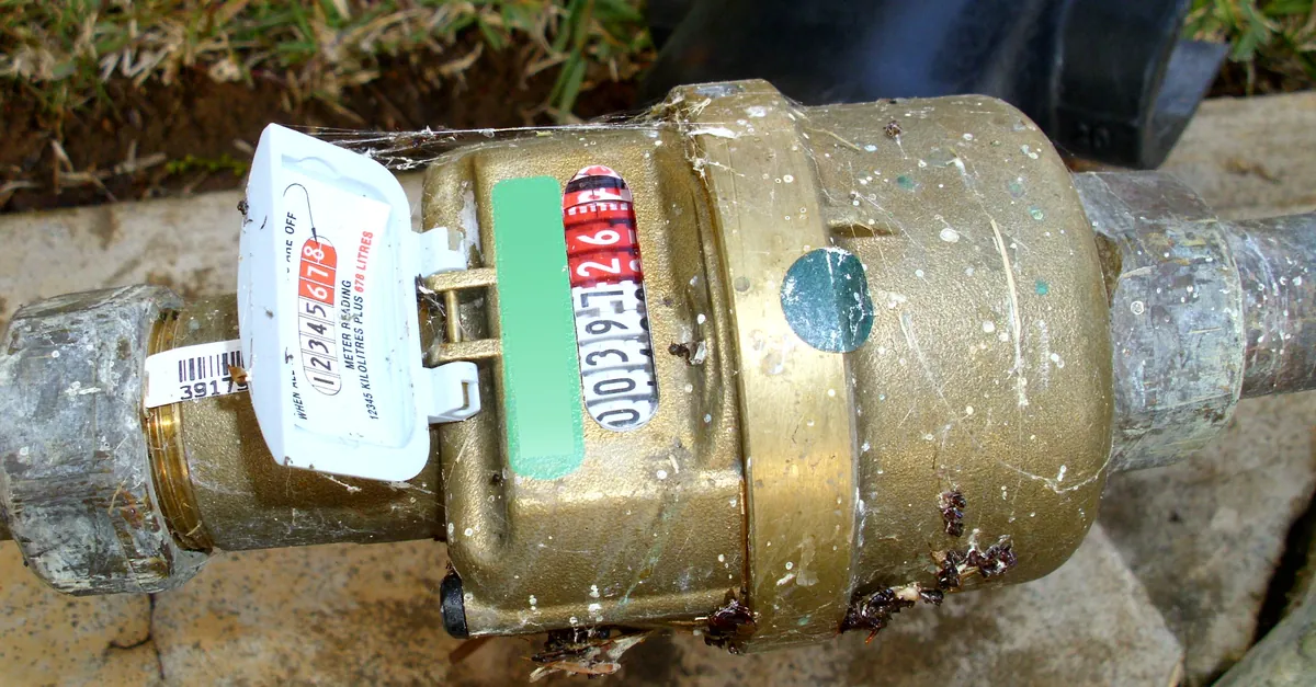 A brass Elster water meter in a lawn with black kilolitre and red litre digits