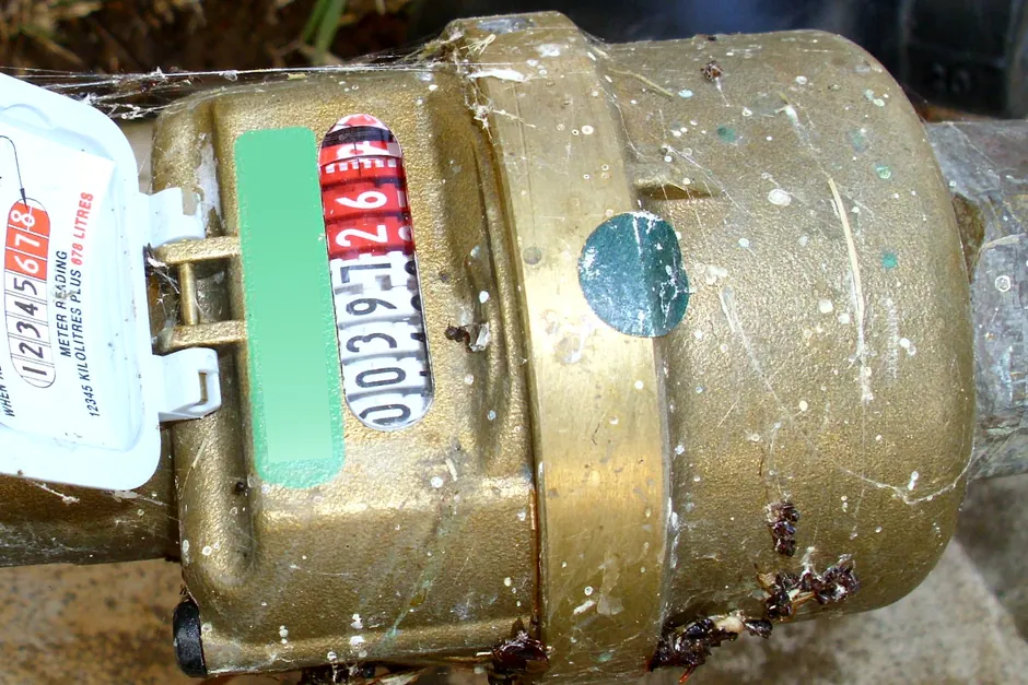 A brass Elster water meter in a lawn showing four black kilolitre digits and three red litre digits